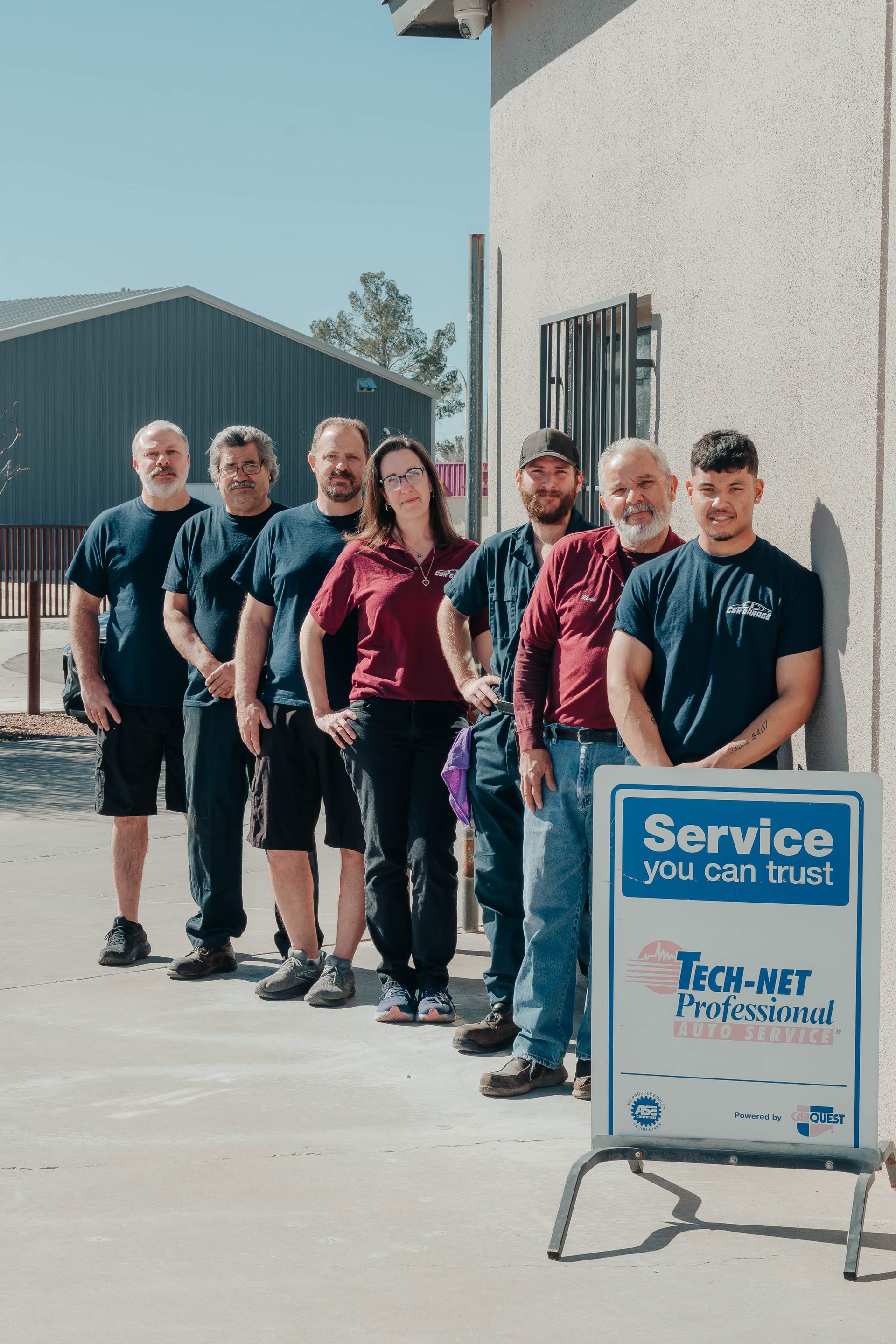 Group of people standing outside by a wall, next to a blue “Service you can trust” signboard.