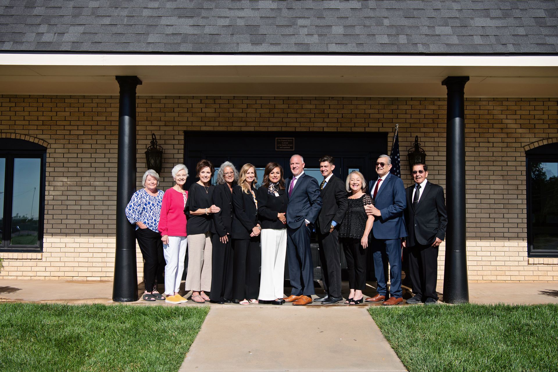 Group of people in formal attire standing outside a building entrance under a covered walkway.