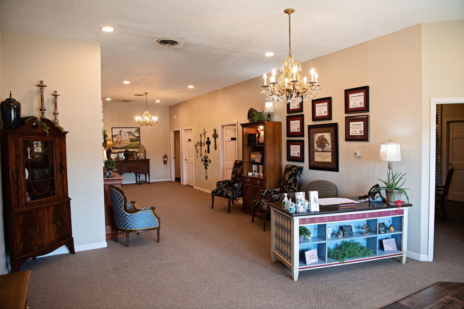 Elegant hallway showroom with chandeliers, framed art, antique furniture, and carpeted floor