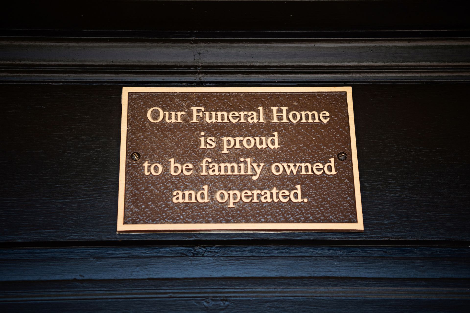 Sign reading “Our Funeral Home is proud to be family owned and operated” on a dark wall.