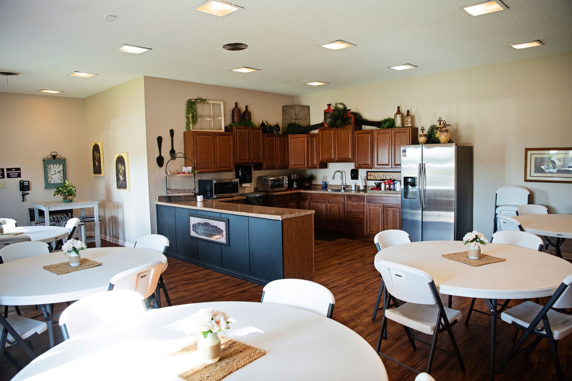 Bright kitchen-dining room with tables, chairs, wooden cabinets, and a stainless steel fridge