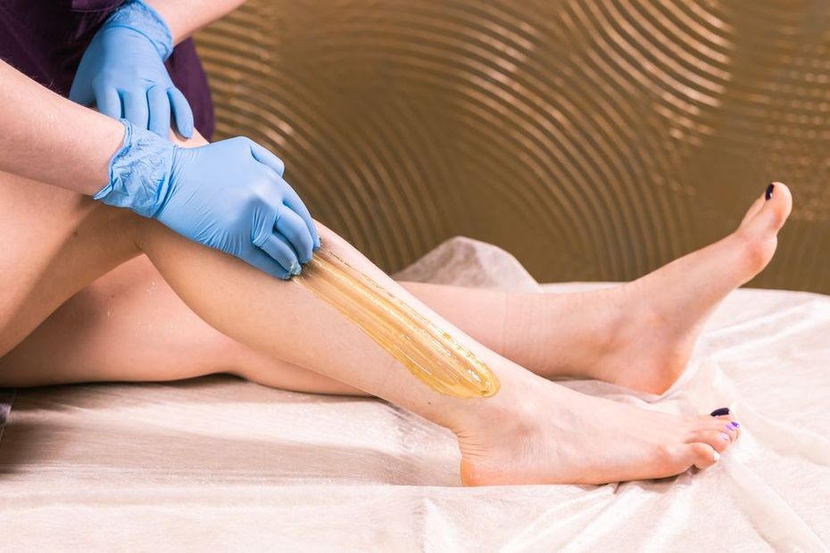 Gloved hands apply wax to a leg during a waxing treatment in a spa setting