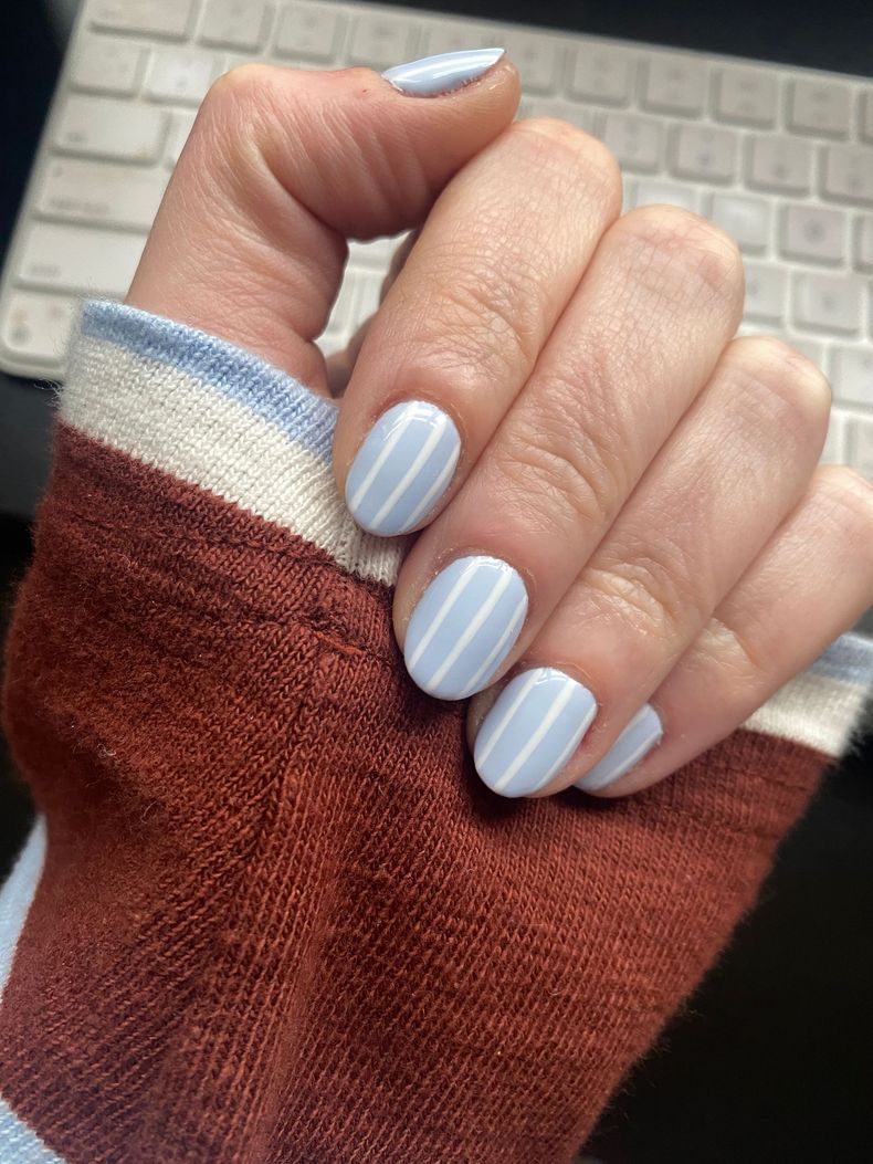 Hand with light blue and white striped manicure over a rust-colored sweater sleeve