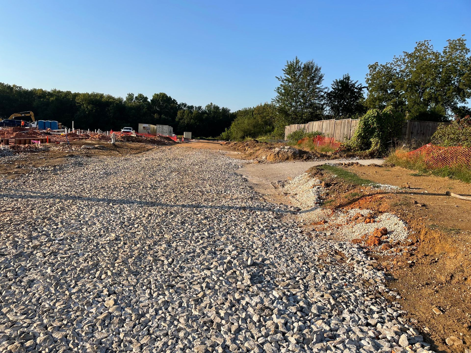 Gravel path under construction, leading towards trees and blue sky on a sunny day.