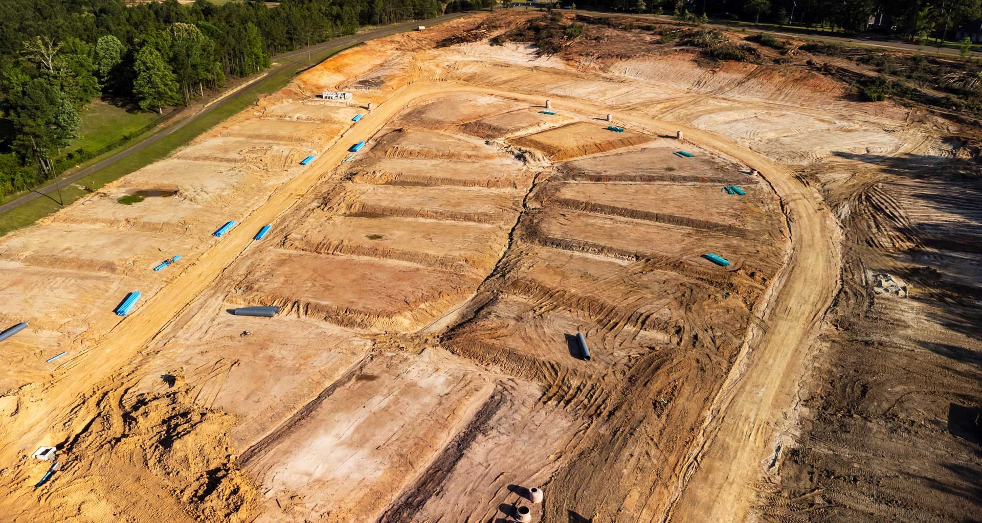 An aerial view of a construction site with a lot of dirt and trees in the background.