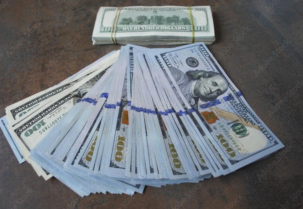Stacks of US $100 bills on a dark surface, one fanned out, one banded together.