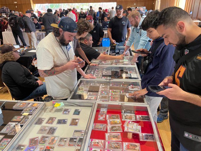 People browse sports cards at a trade show, looking at cards in display cases.