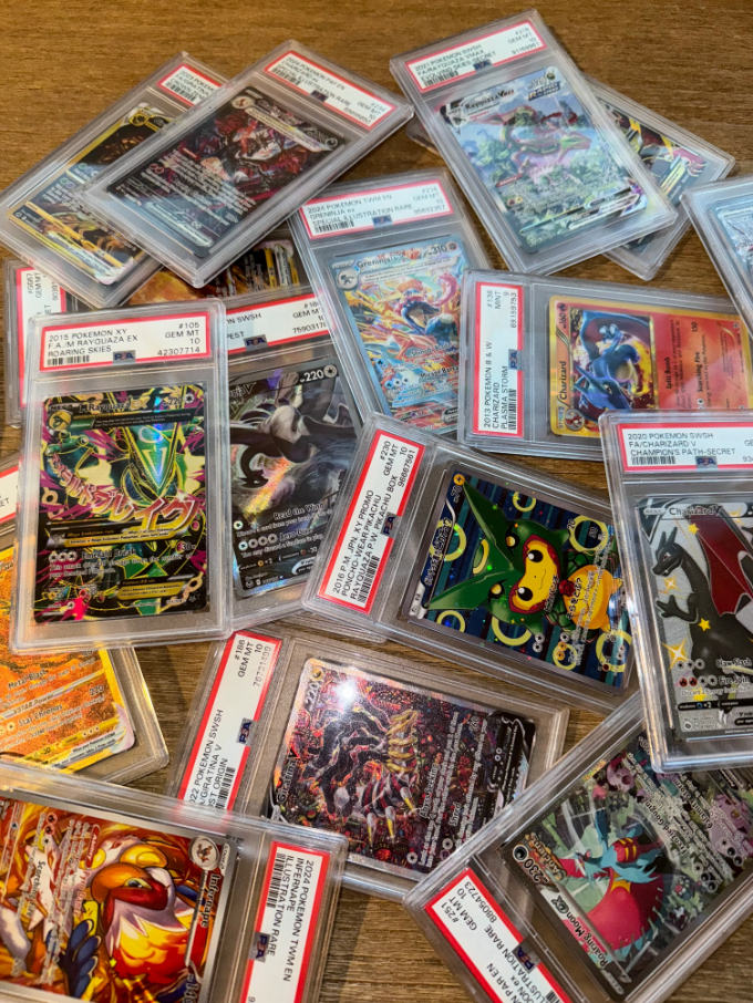 A collection of graded Pokémon trading cards scattered on a wooden surface.