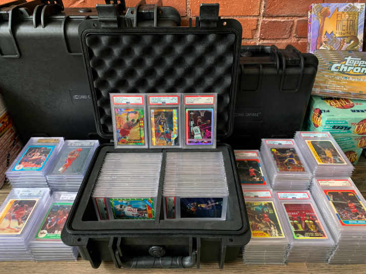 Collection of graded sports cards in cases, some displayed inside a black carrying case, alongside unopened boxes.
