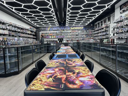 Interior of a card game store with tables for playing and display shelves filled with card packs.