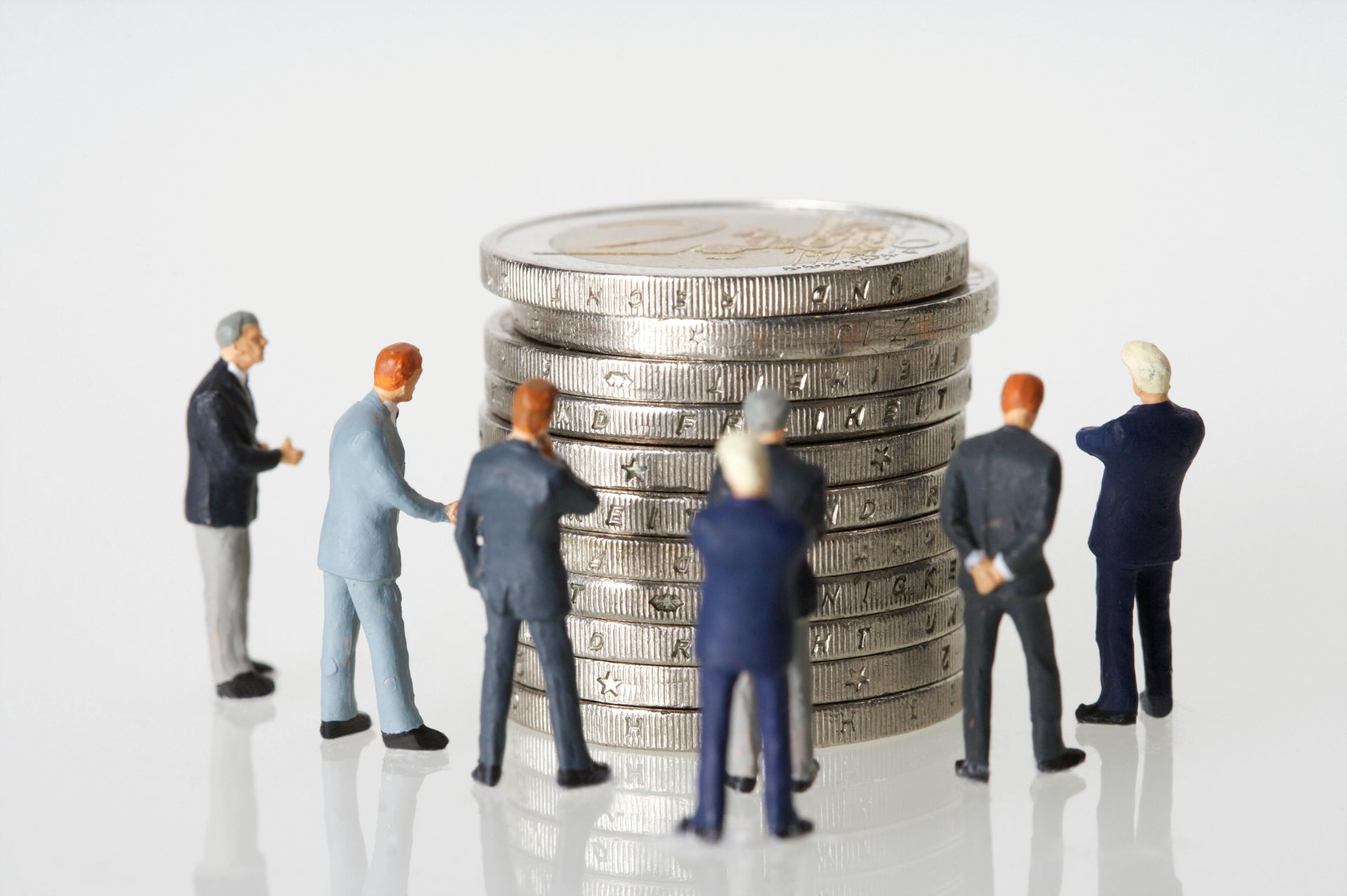 Miniature figures in suits gather around a tall stack of coins.