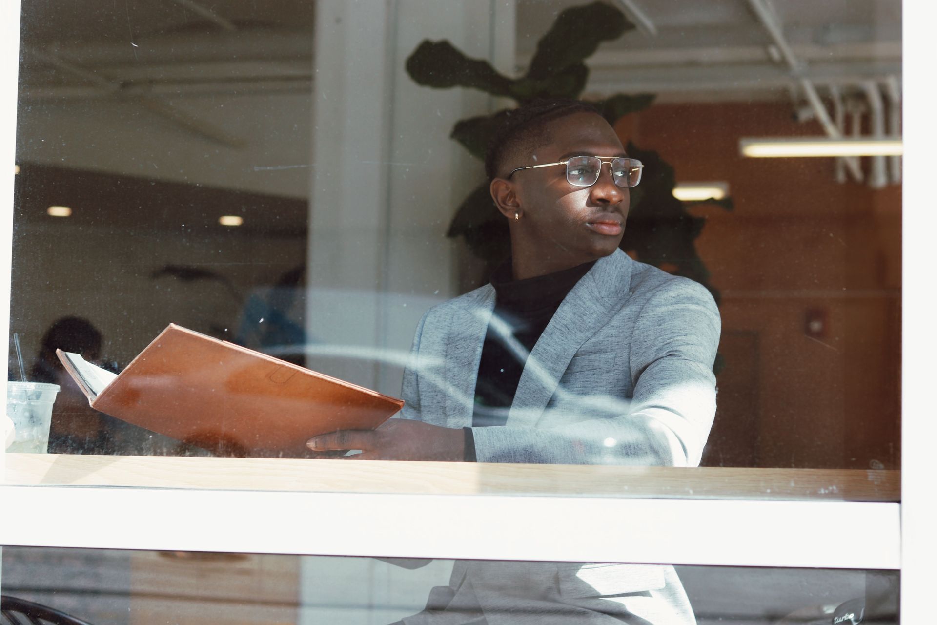 Person in glasses holding a folder, looking out a window in an office.