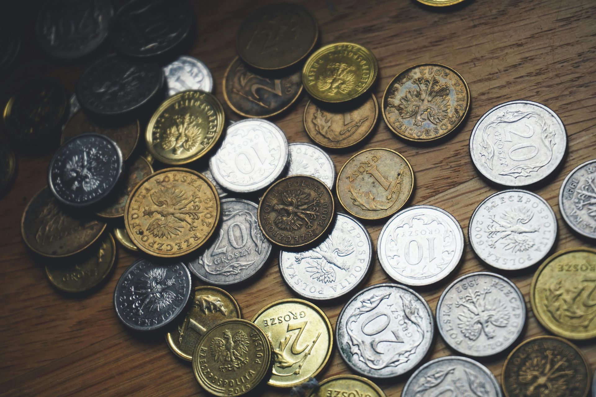 A scattered collection of gold and silver coins of various sizes resting on a wooden surface.