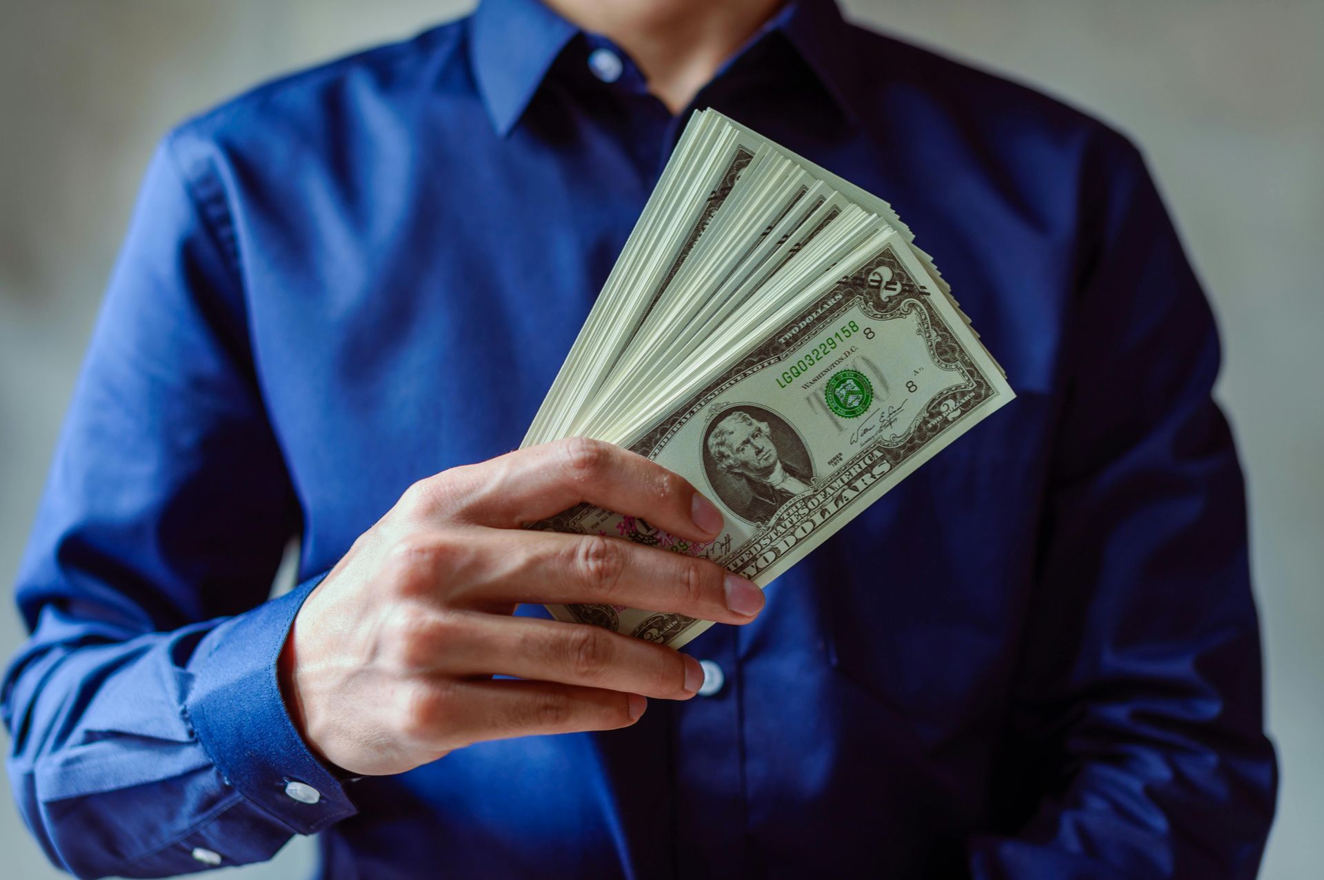 Person in blue shirt holding a fan of U.S. dollar bills
