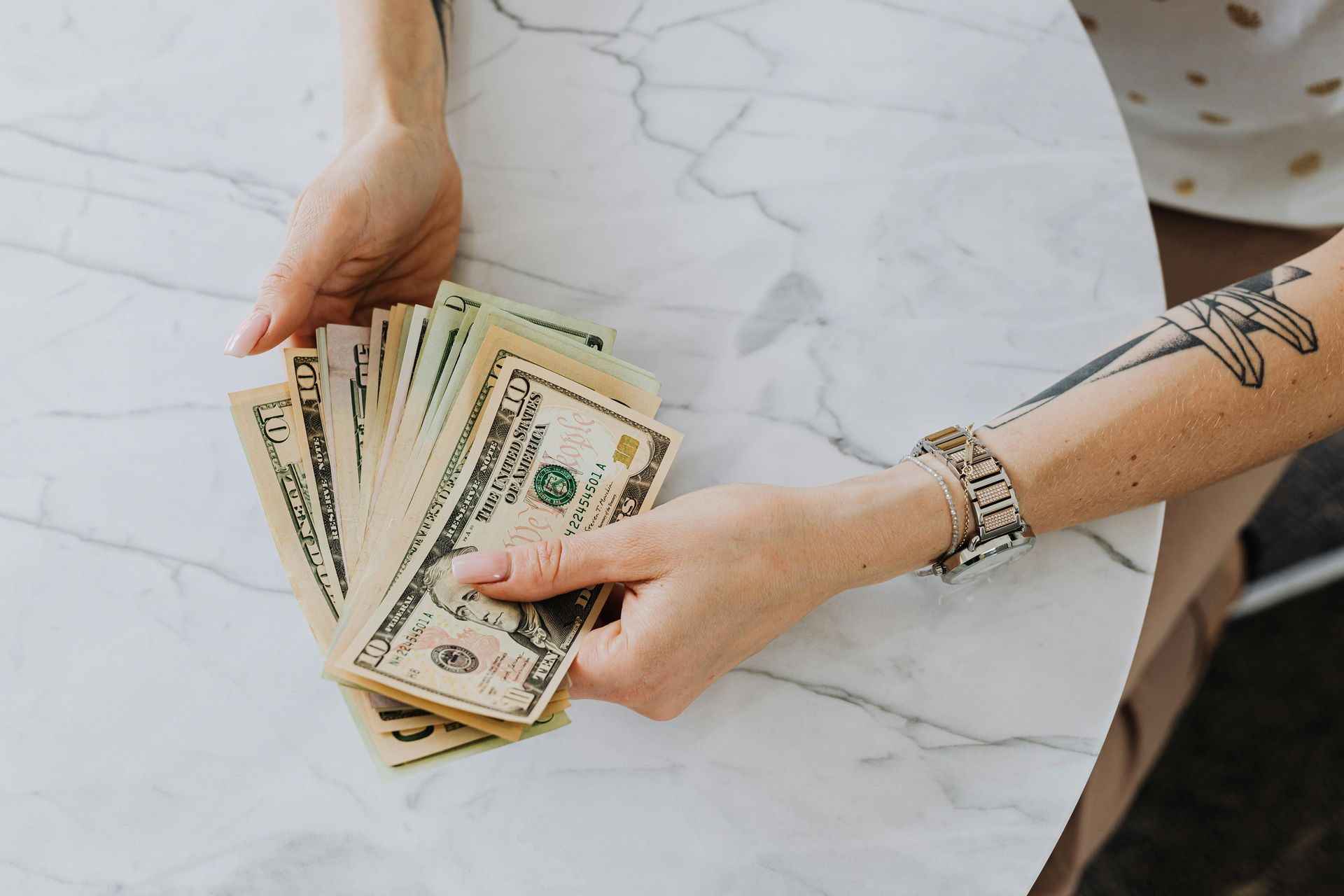 Hands holding a fanned stack of US dollar bills on a marble table.
