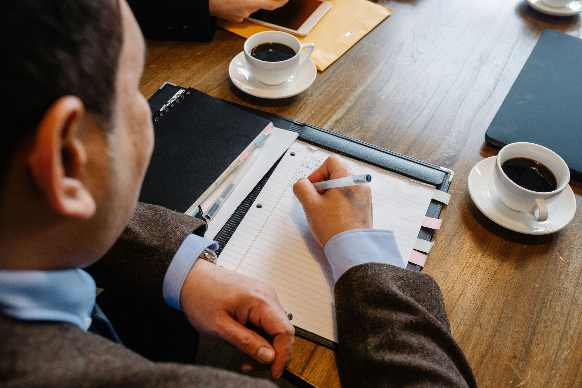 People reviewing documents and writing notes at a wooden table with coffee cups