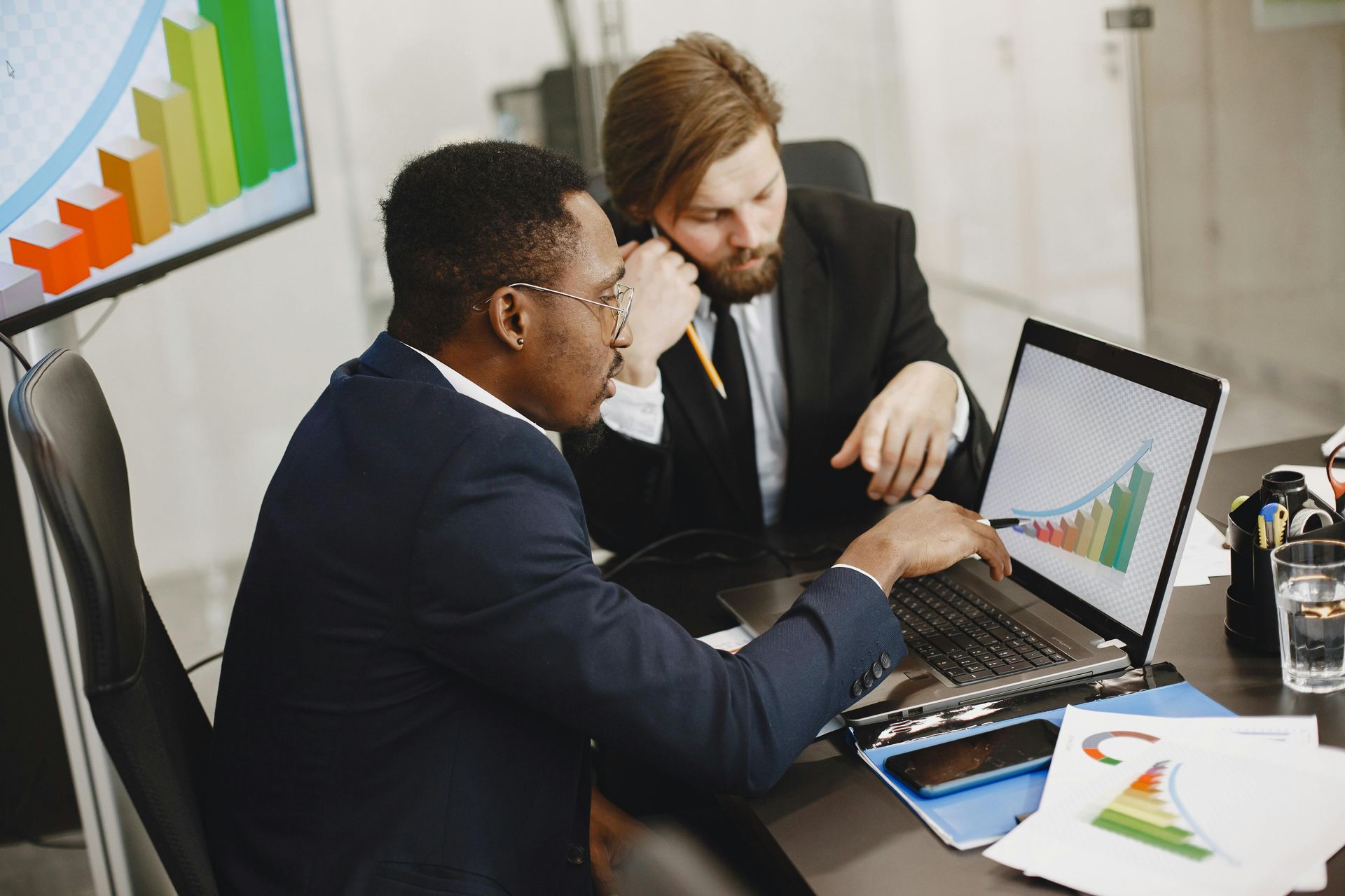 Two professionals in suits reviewing positive growth charts on a laptop screen in a bright, modern office.
