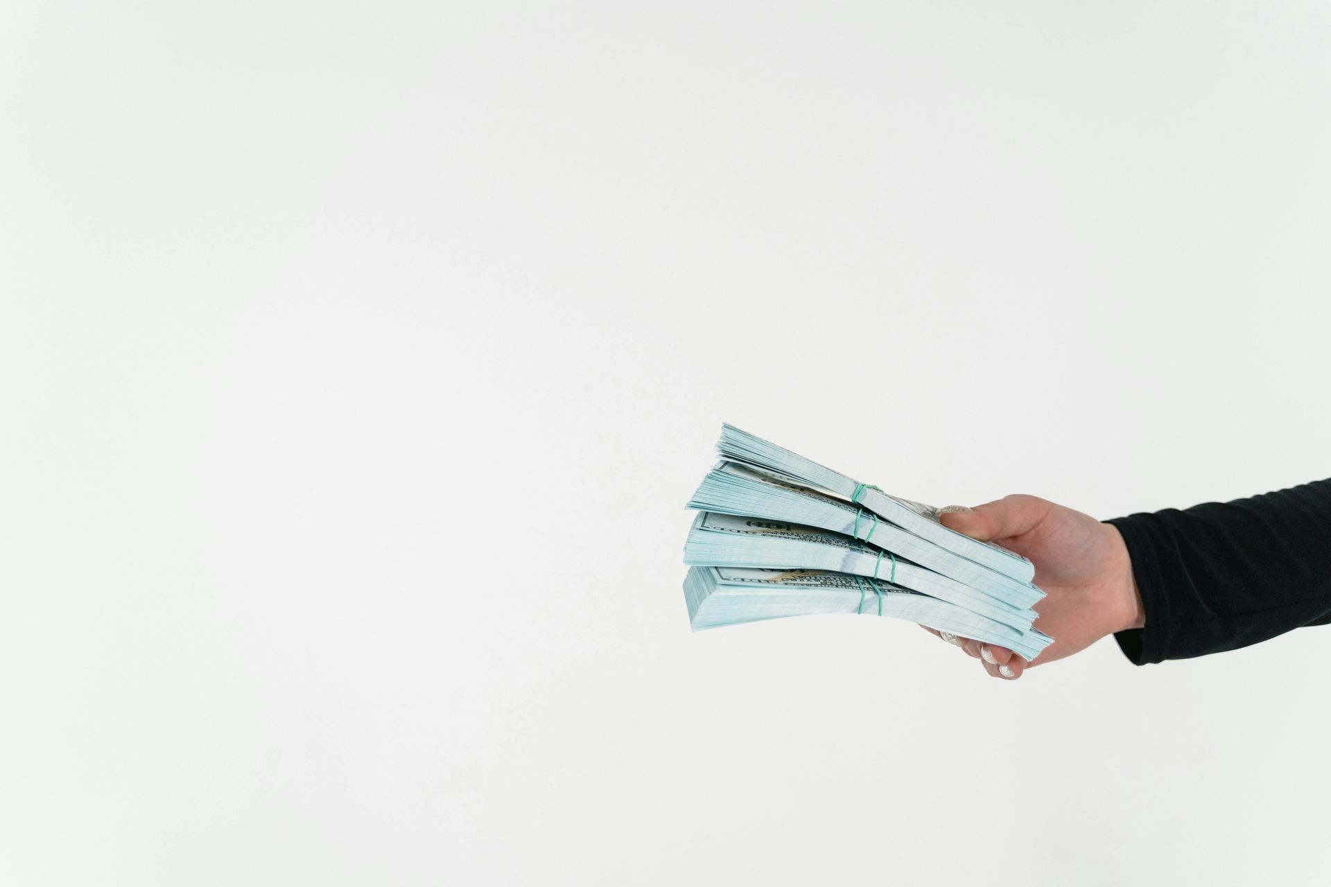 A hand wearing a black sleeve holding a thick stack of blue currency against a white background.