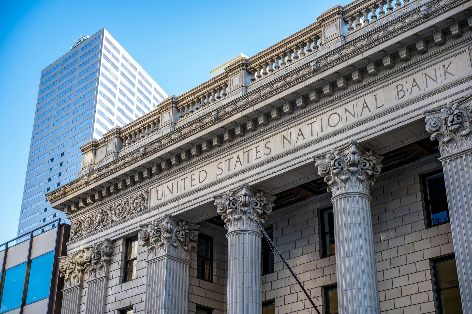 United States National Bank building facade with stone columns beside a modern glass skyscraper