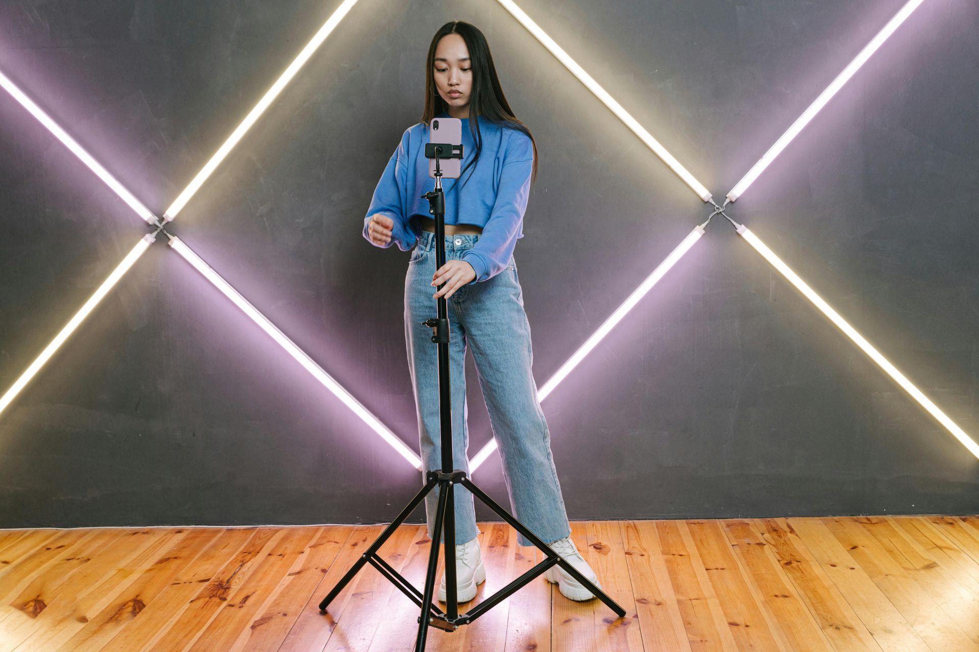 Woman adjusting smartphone on tripod in front of a neon-lit wall.