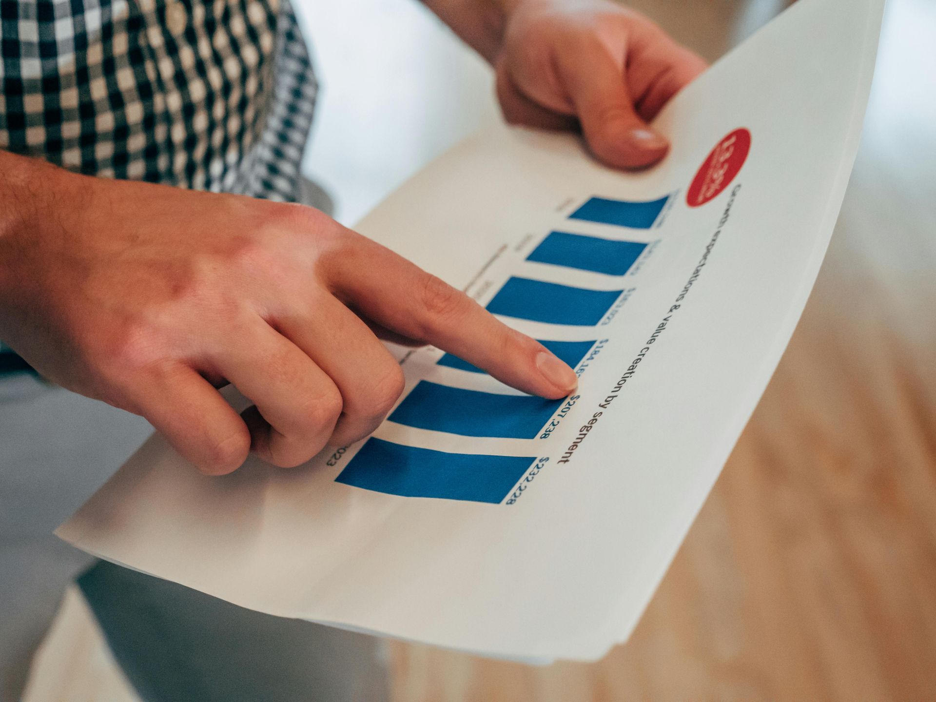 A close-up of a person's hand pointing to a blue bar graph on a document.