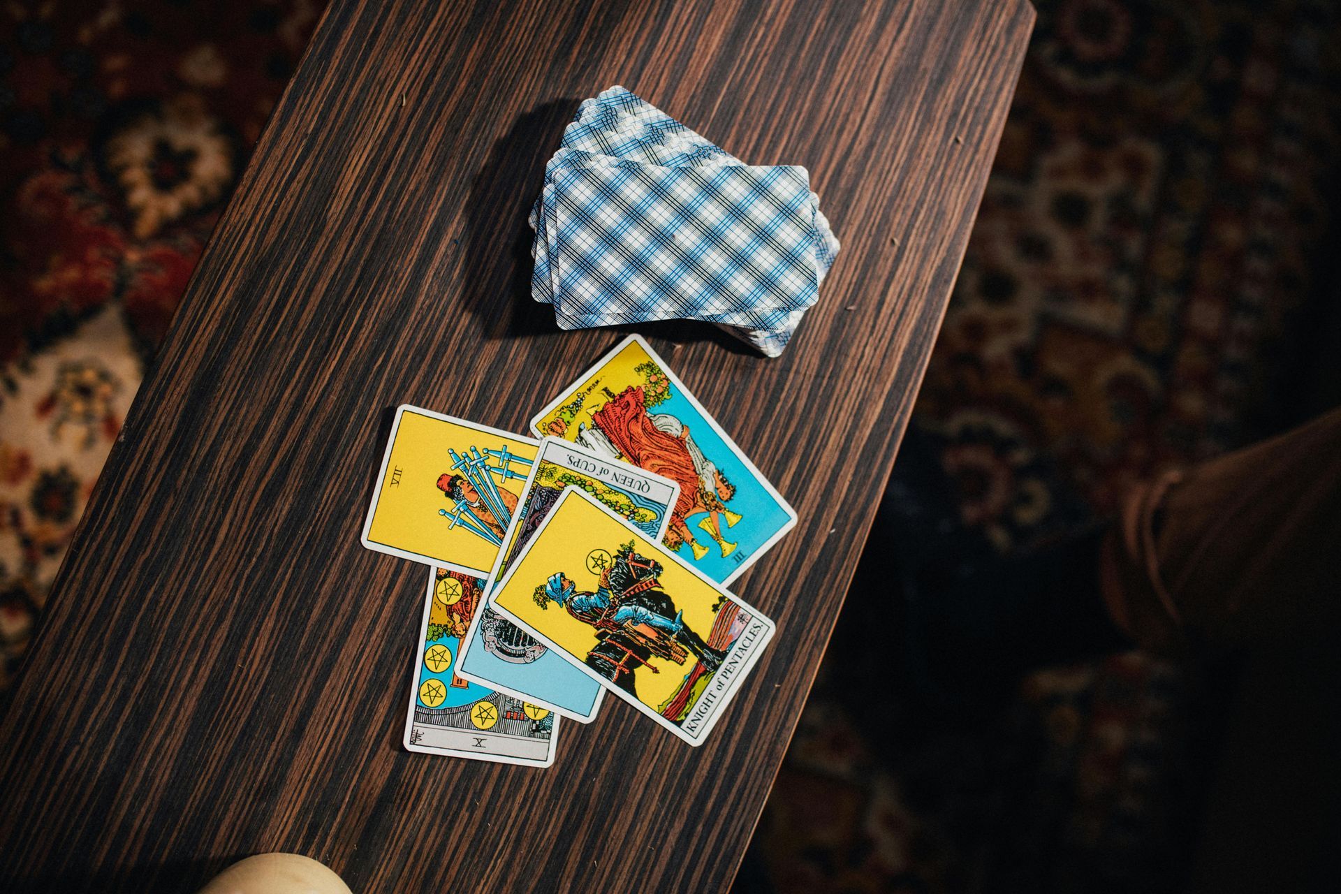 A small deck of tarot cards, including several face-up cards, lies on a dark wooden table.