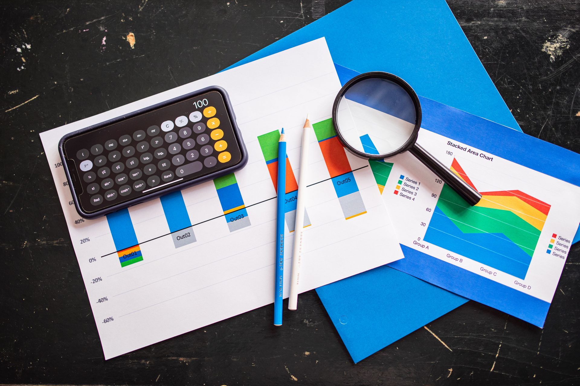 Calculator, magnifying glass, and pens on financial charts with blue folders.