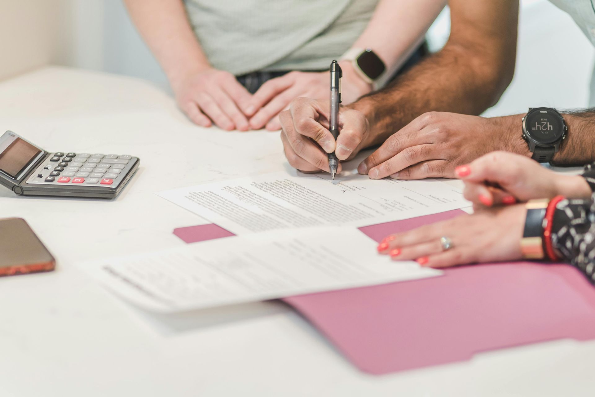 People signing documents at a table; calculator and phone nearby.