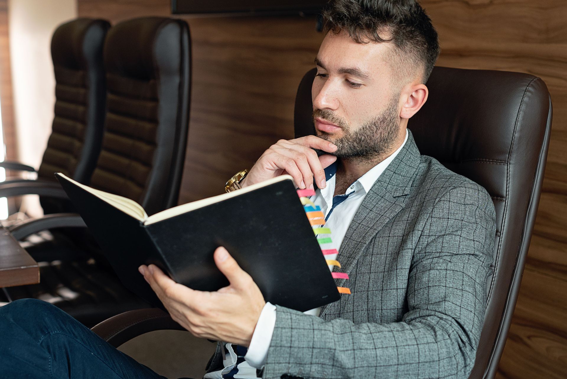 Man in a gray blazer reading a book at a conference table in an office setting
