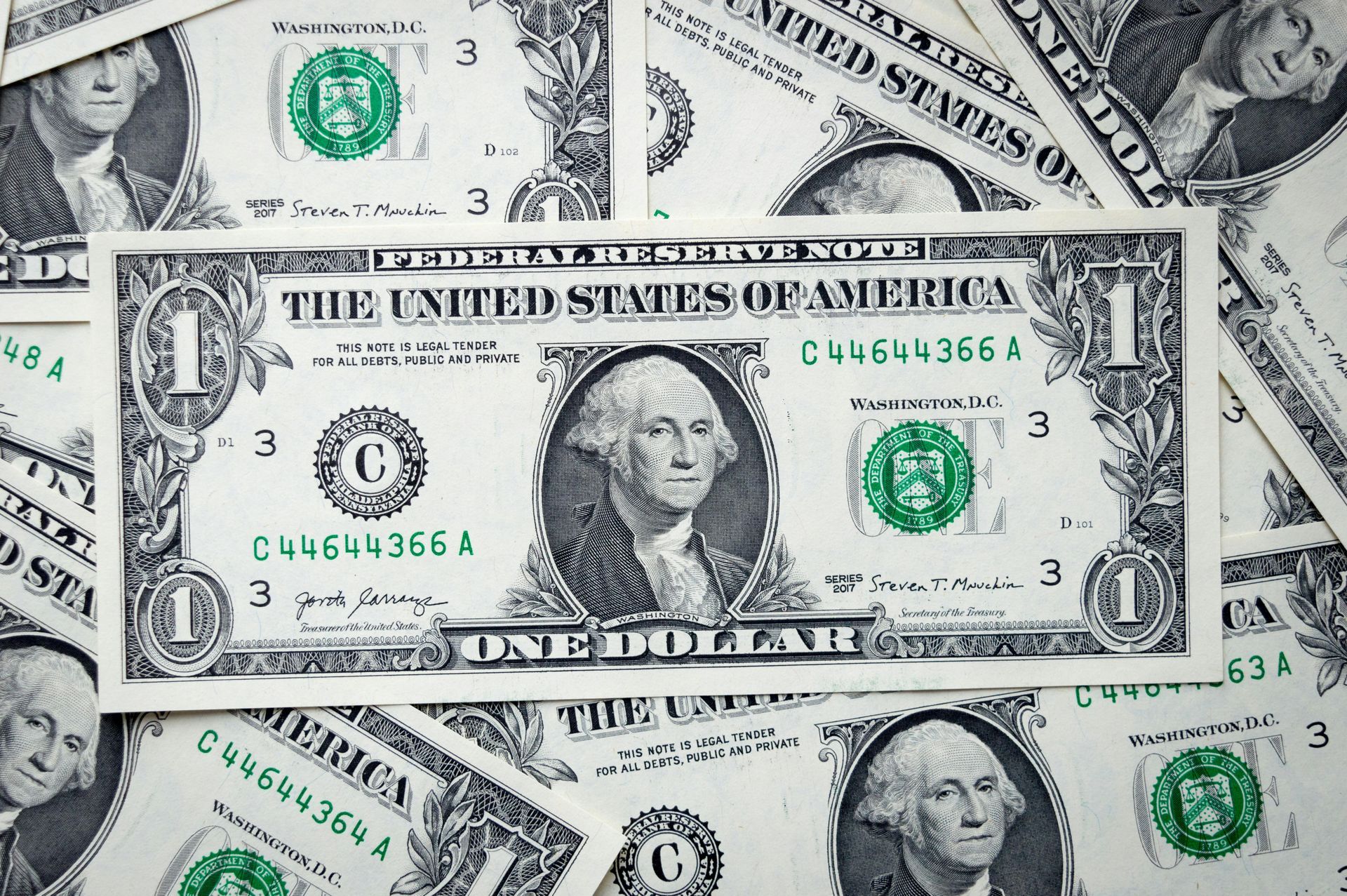 Stack of U.S. one-dollar bills scattered on a light background.