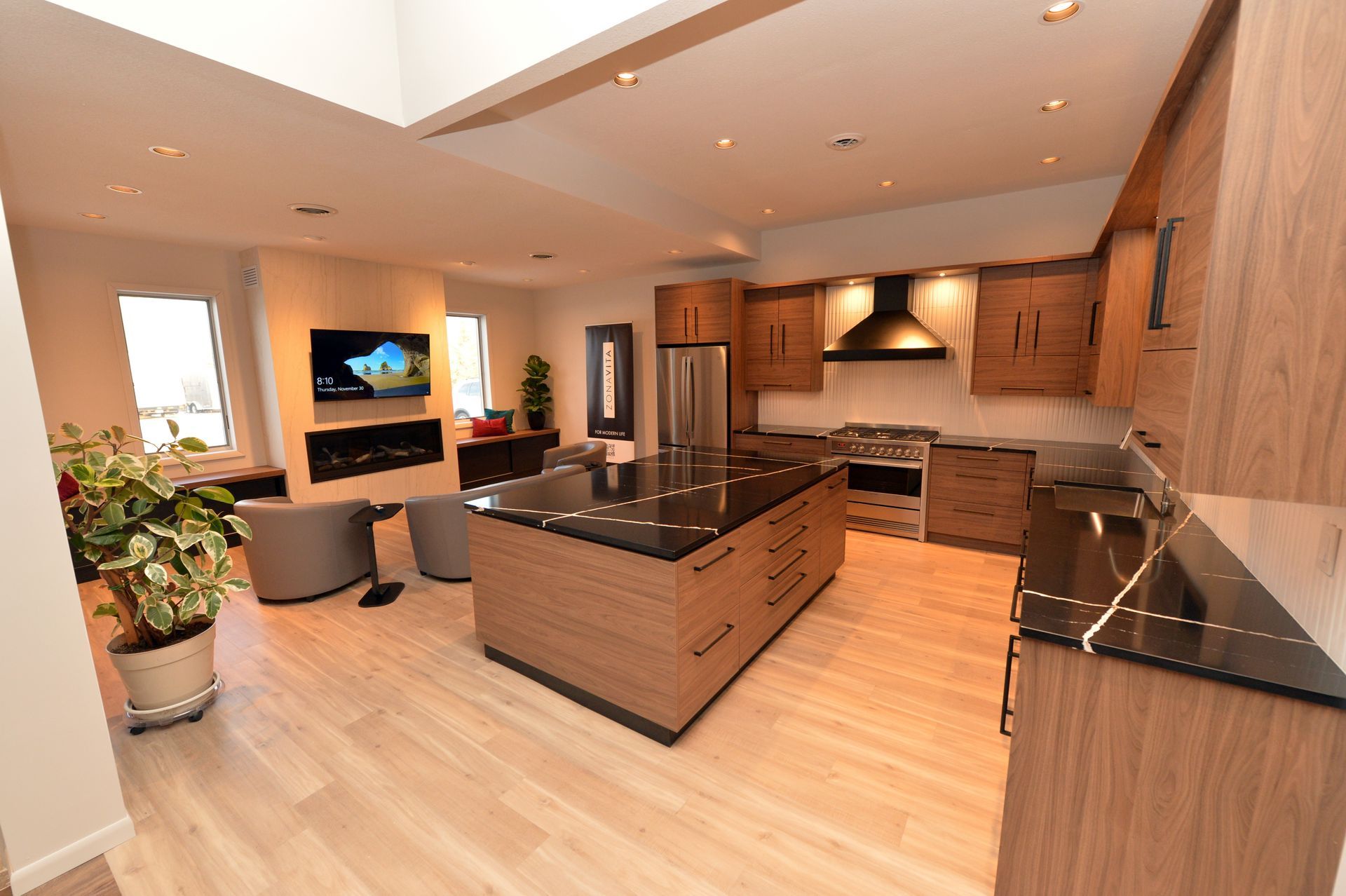 Modern open-plan kitchen with wood cabinets, black countertops, island, and light wood floors