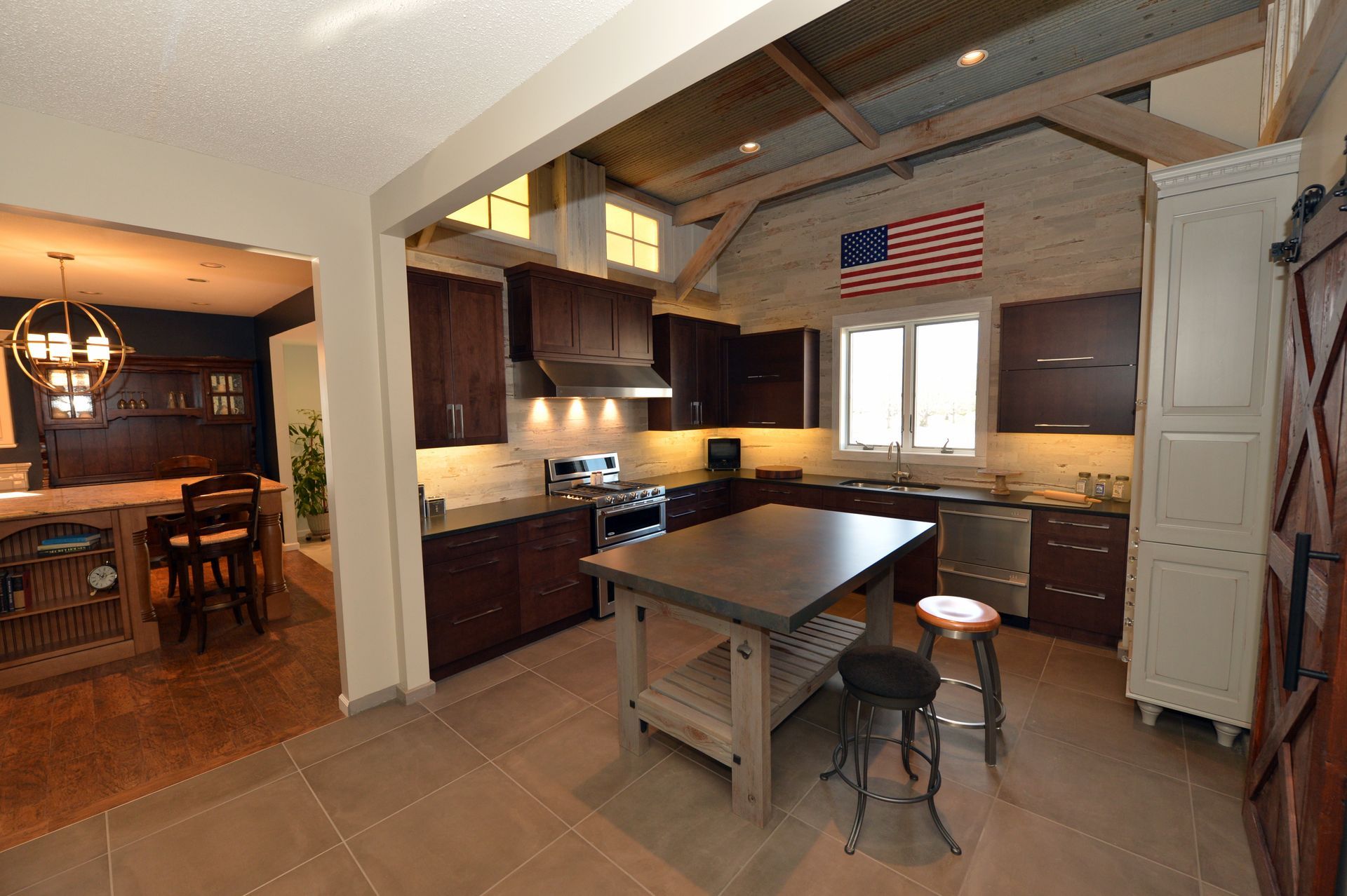 Modern kitchen with island, wood cabinets, stainless appliances, and an American flag over the window.