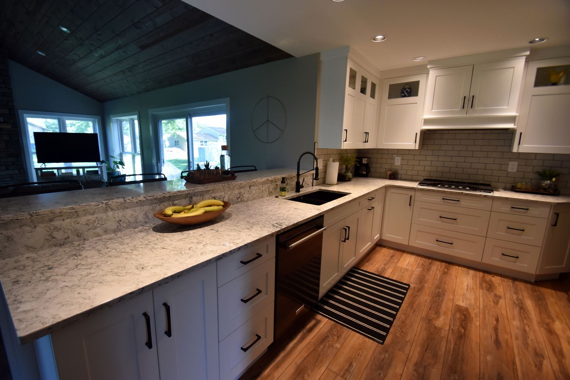 Modern kitchen with granite island, white cabinets, wood floors, and large windows overlooking the outdoors