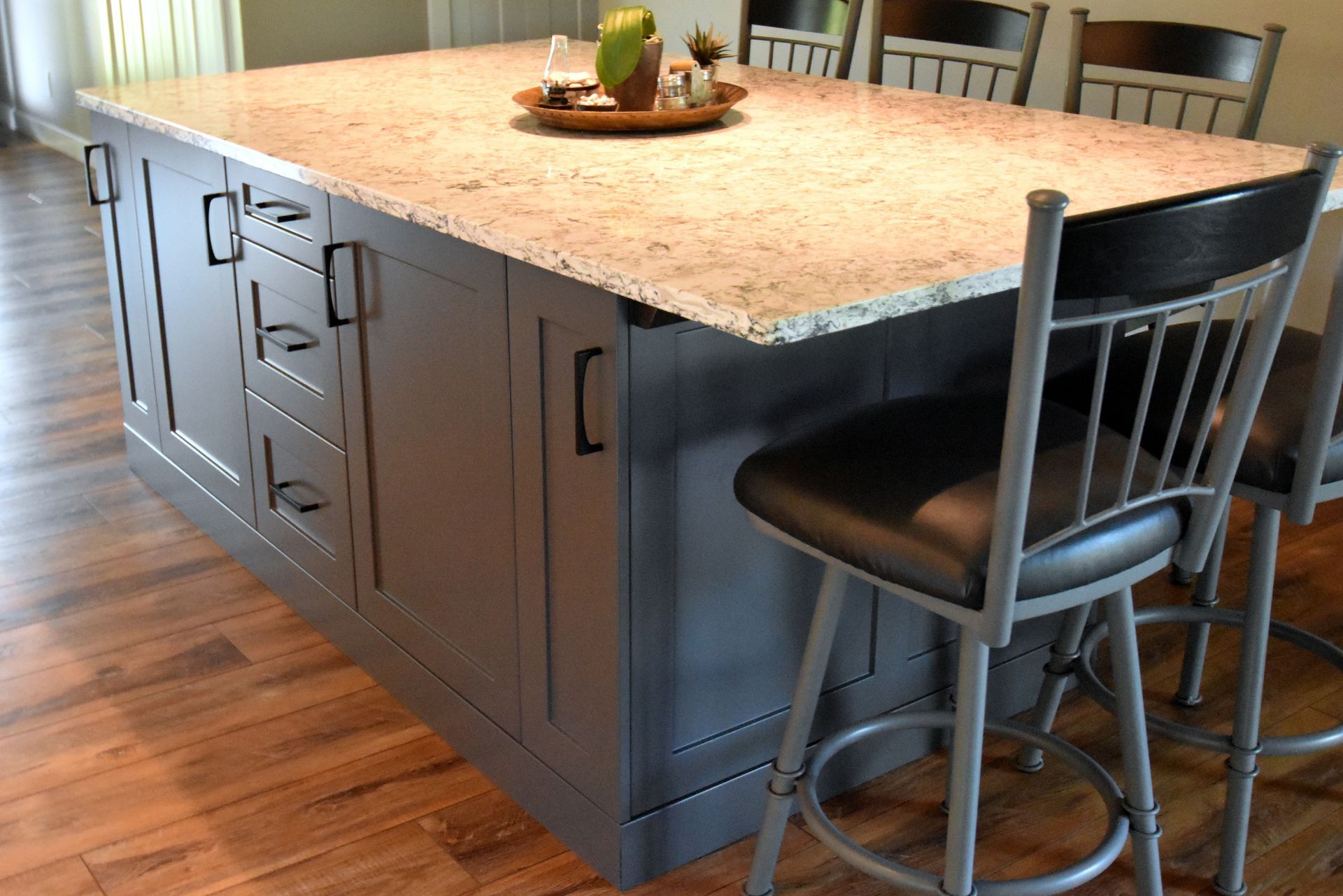 Kitchen island with dark cabinets, stone countertop, and two metal bar stools in a hardwood-floor kitchen
