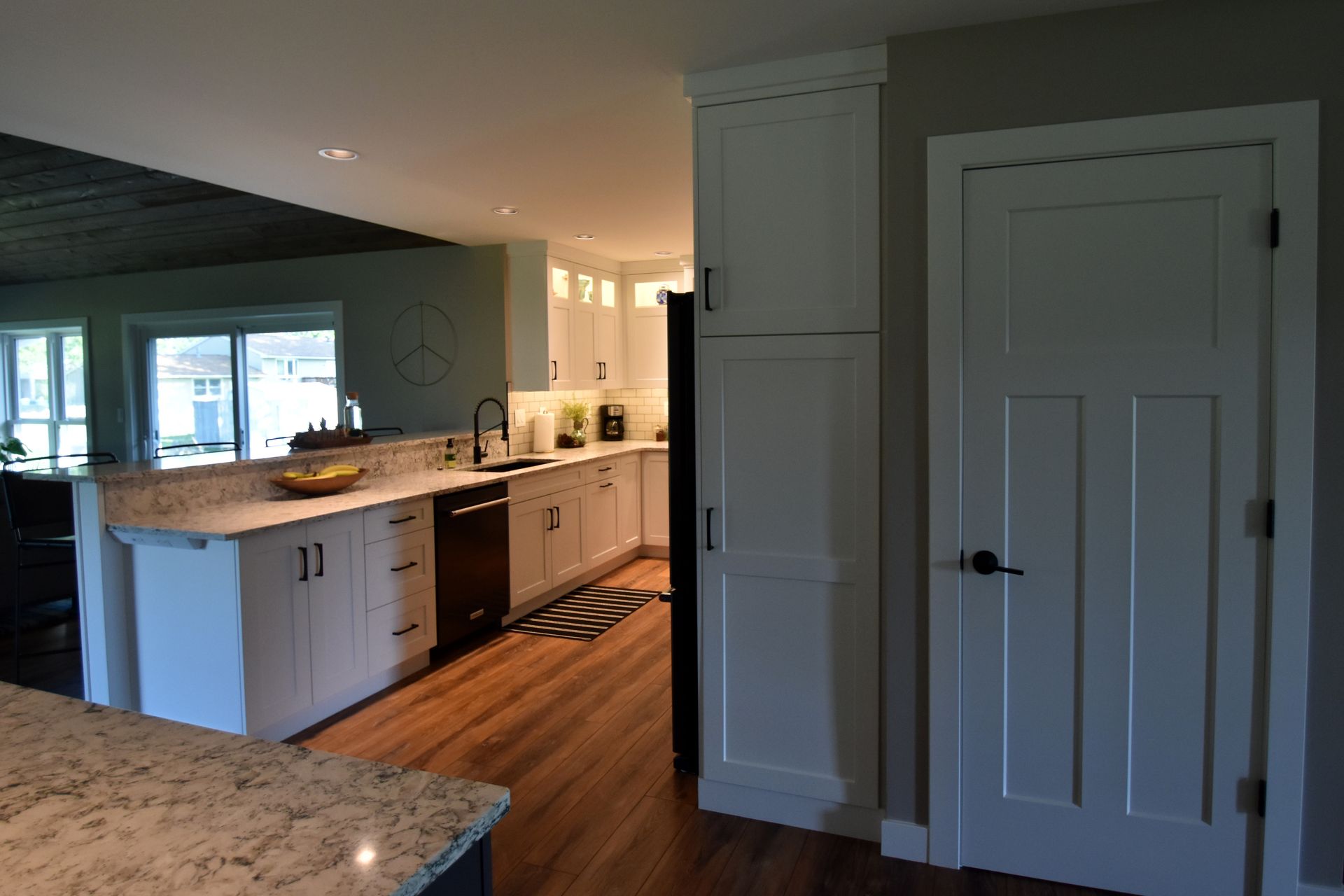 Modern kitchen with white cabinets, granite counters, wood floors, and a door on the right.