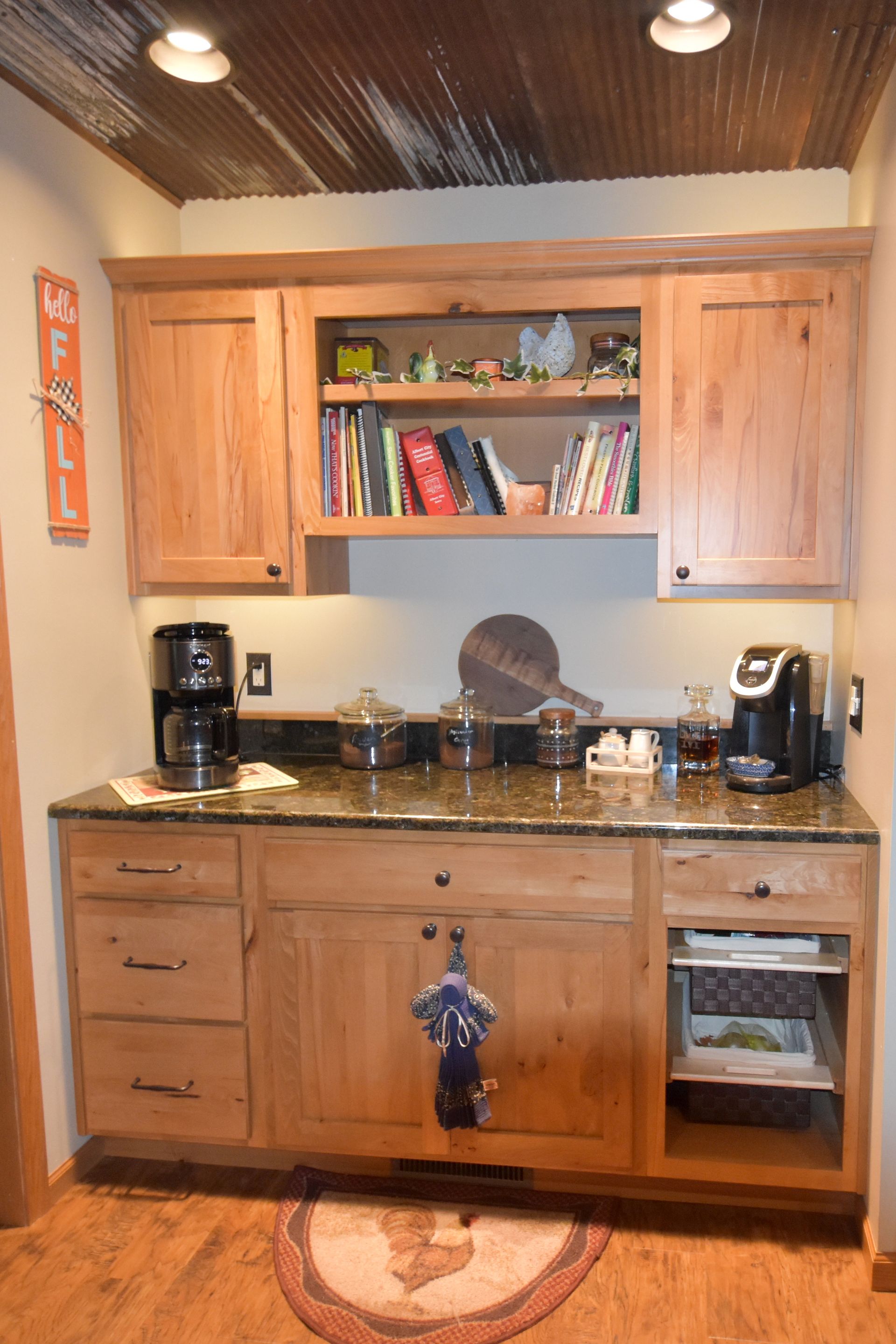 Kitchen nook with wooden cabinets, black countertop, and coffee maker under warm ceiling lights