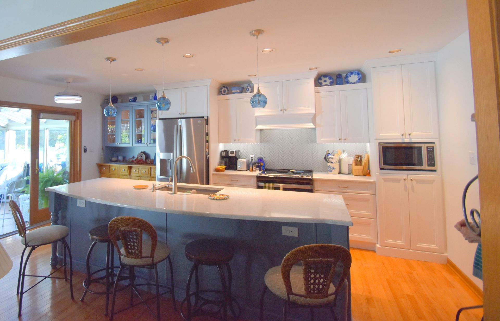 Bright kitchen with white cabinets, stainless fridge, blue pendant lights, and a large island with stools