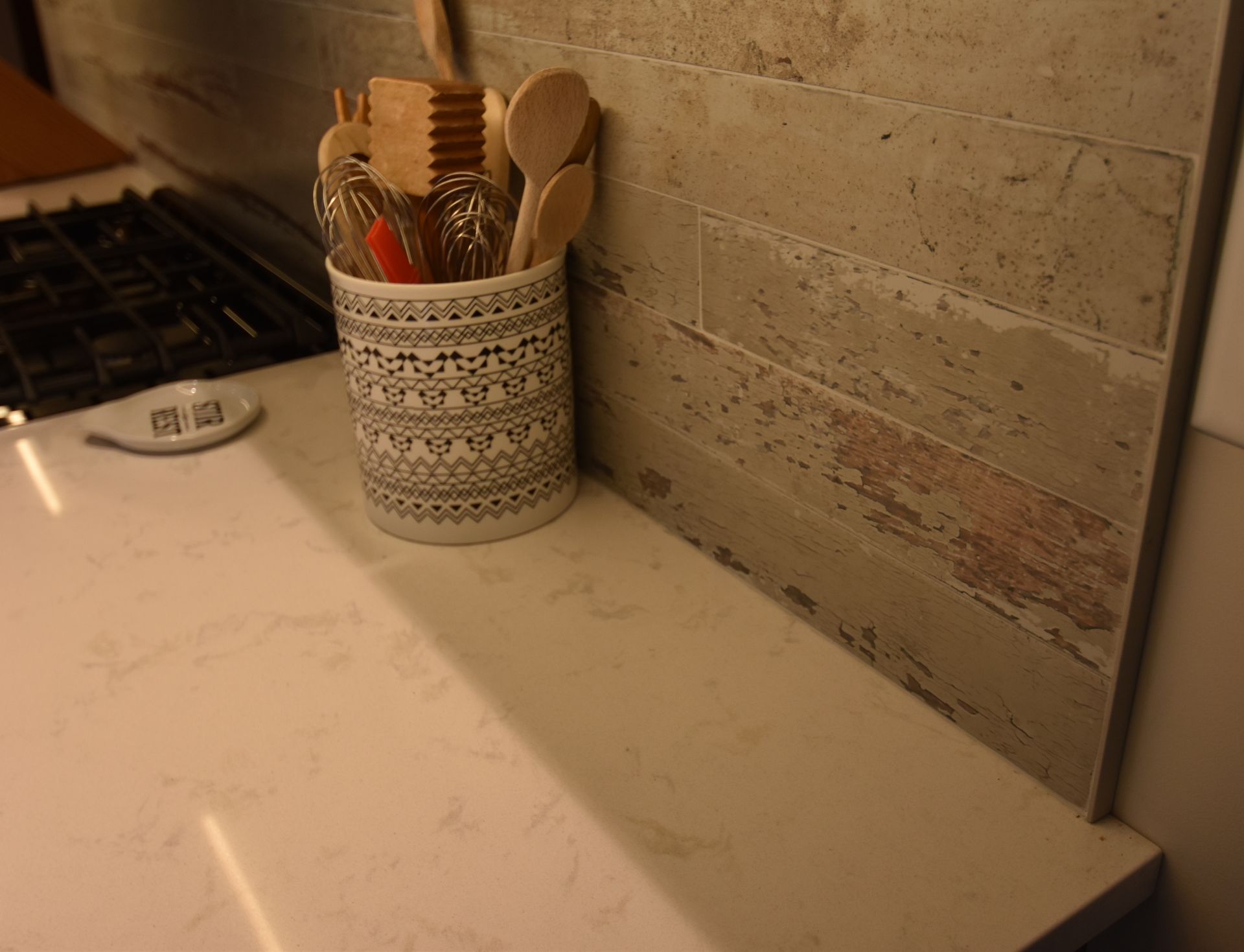 Kitchen counter with utensil holder, wooden spoons, and a gas stove beside a beige tiled backsplash.