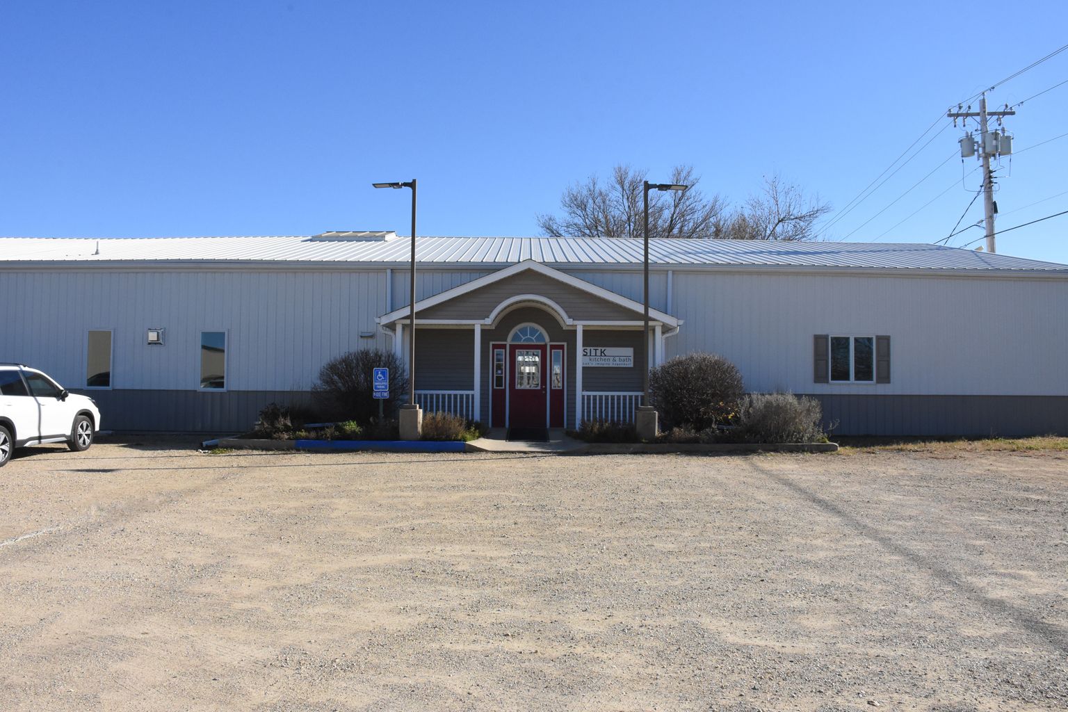 Small single-story building with a red entrance door, gravel lot, and blue sky in front.