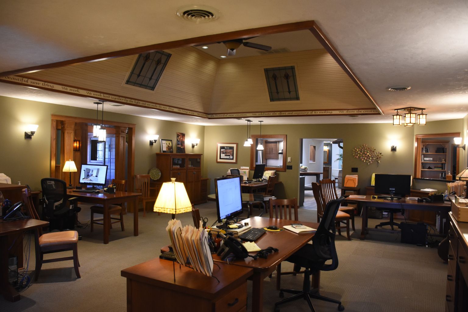 Warm office lobby with desks, lamps, computer monitors, and wood-paneled ceiling