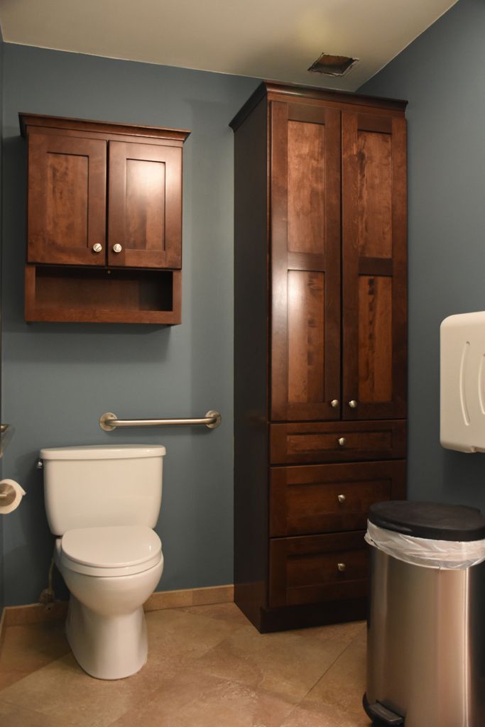 Small bathroom with toilet, wall cabinet, tall wood storage cabinet, towel bar, and trash can.