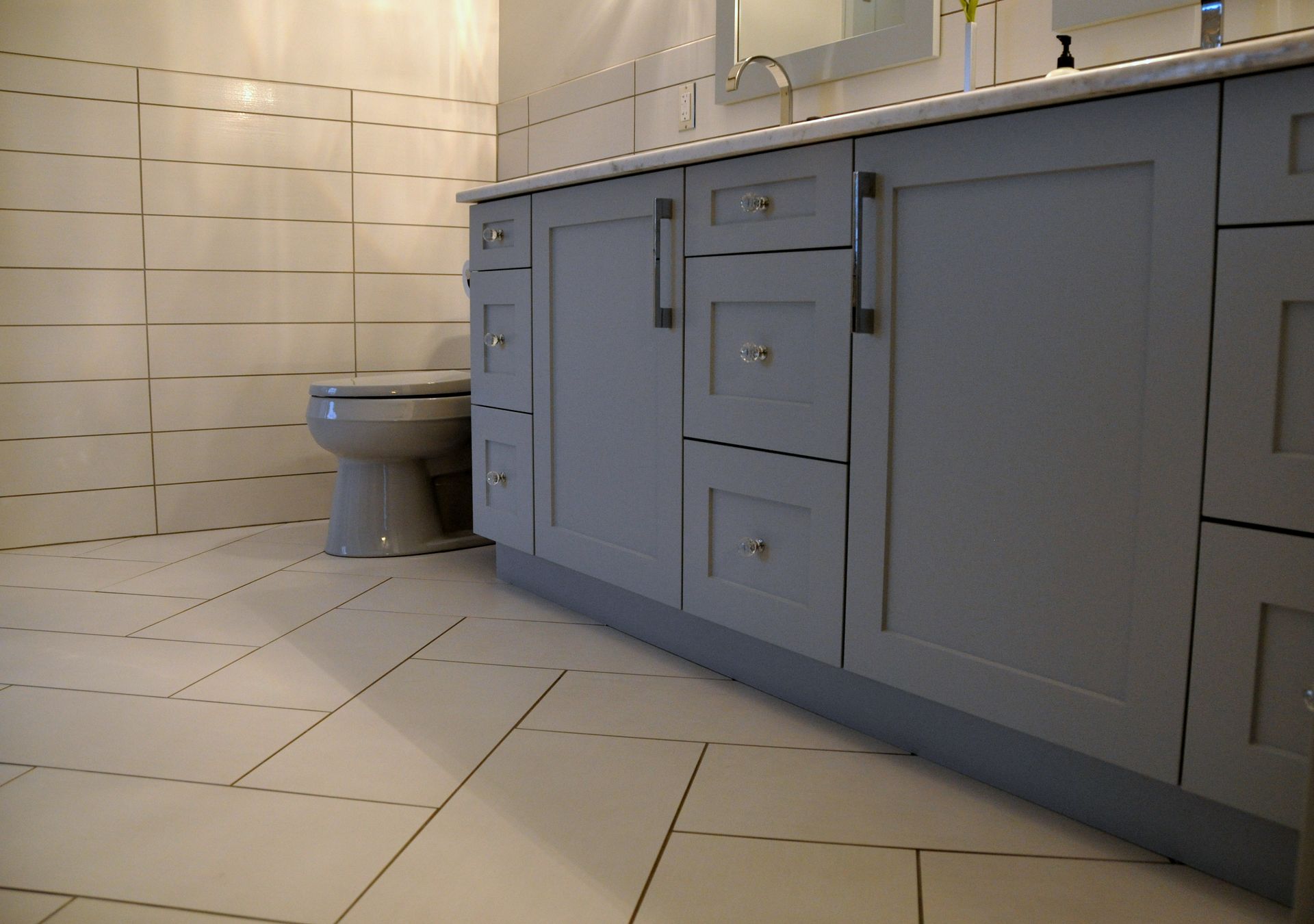 Tiled bathroom with blue vanity cabinets and a toilet beside them.