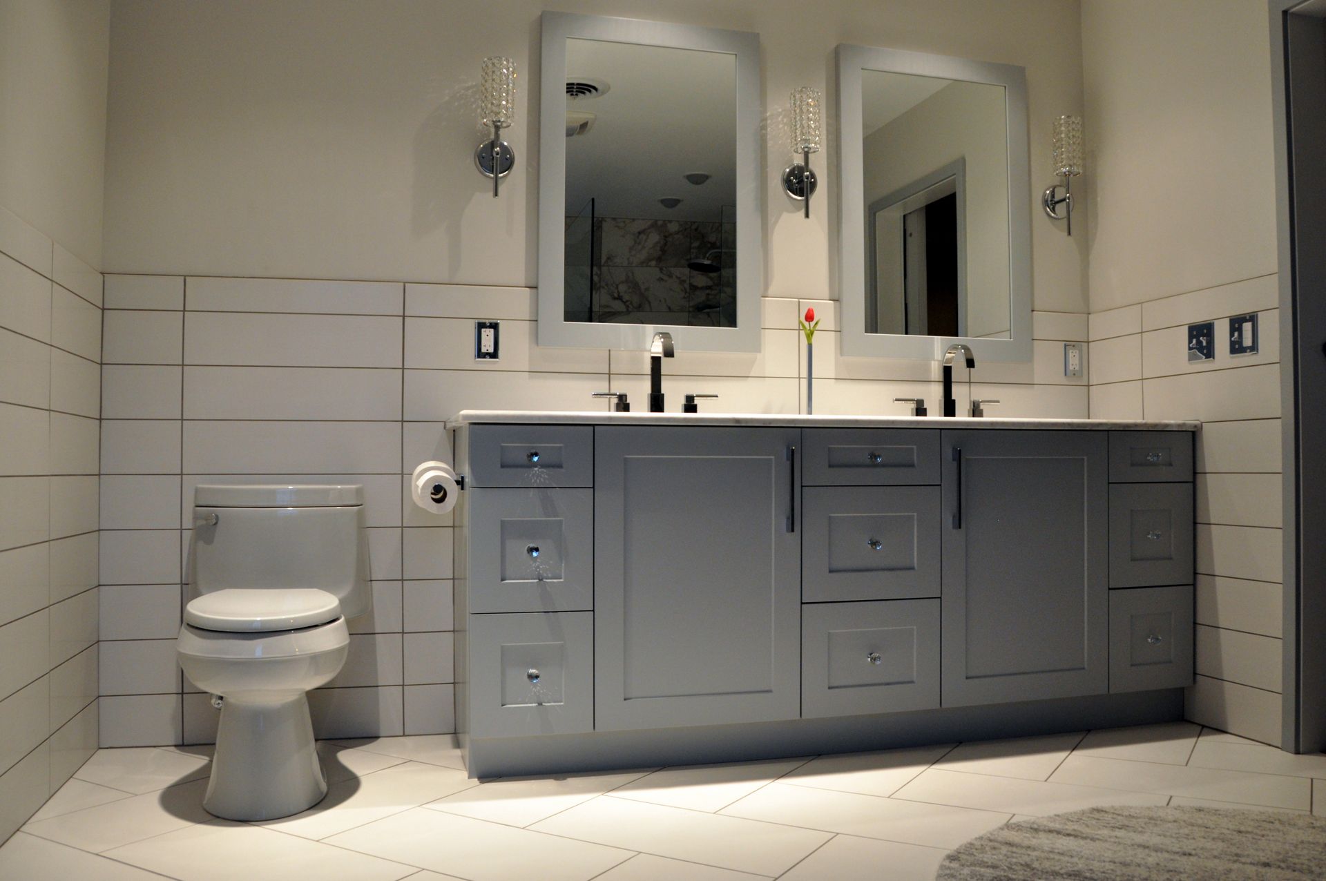 Modern bathroom with gray vanity, double sinks, mirrors, and a white toilet beside tiled walls.