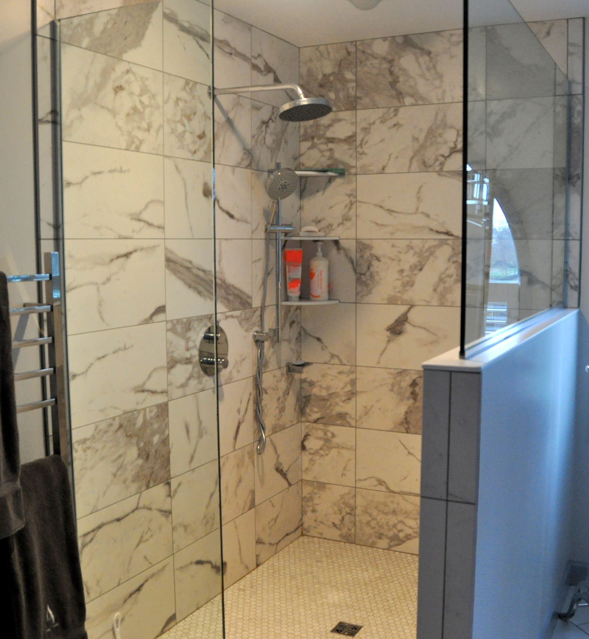 Modern shower with marble tile, glass enclosure, rainfall showerhead, and built-in shelf.