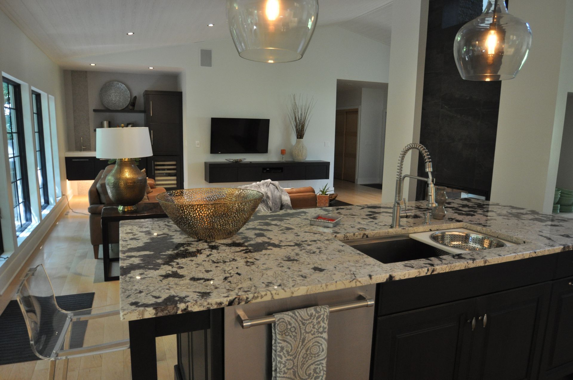 Modern kitchen with marble island, pendant lights, and open view to a living room with TV and fireplace.