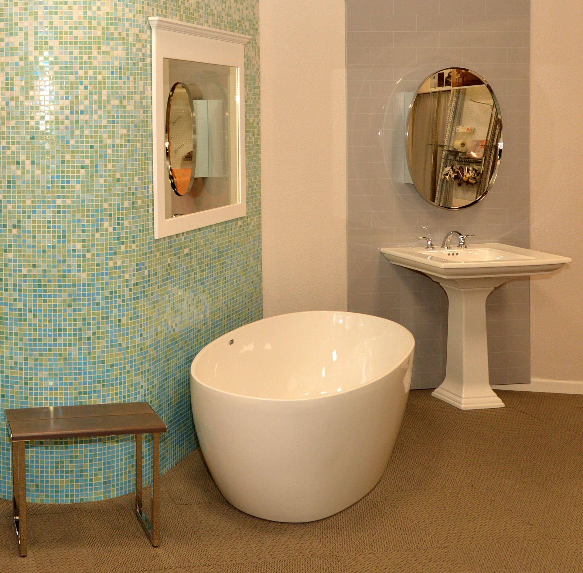 Modern bathroom with mosaic tile wall, white oval tub, pedestal sink, and round mirror