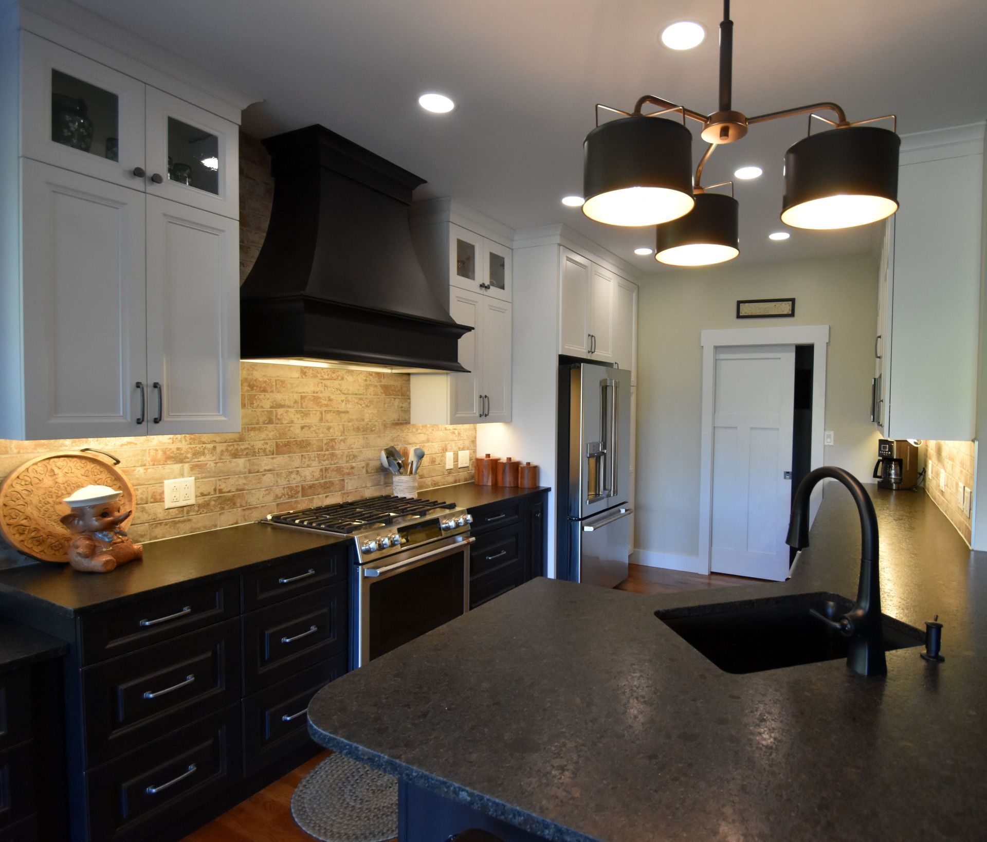 Modern kitchen with dark granite island, white cabinets, black range hood, and pendant lights