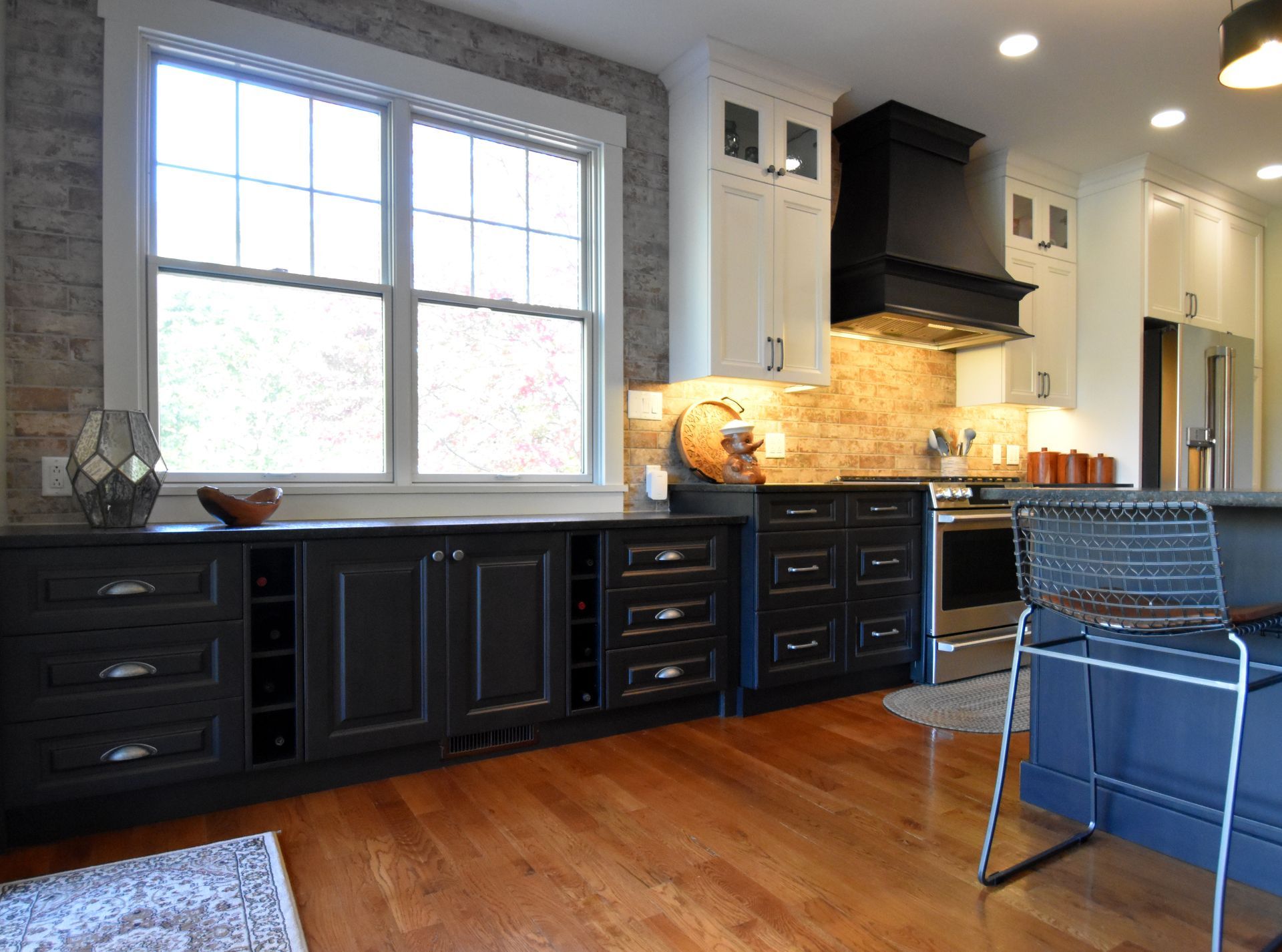 Modern kitchen with dark cabinets, large window, stone backsplash, and blue chair on hardwood floor