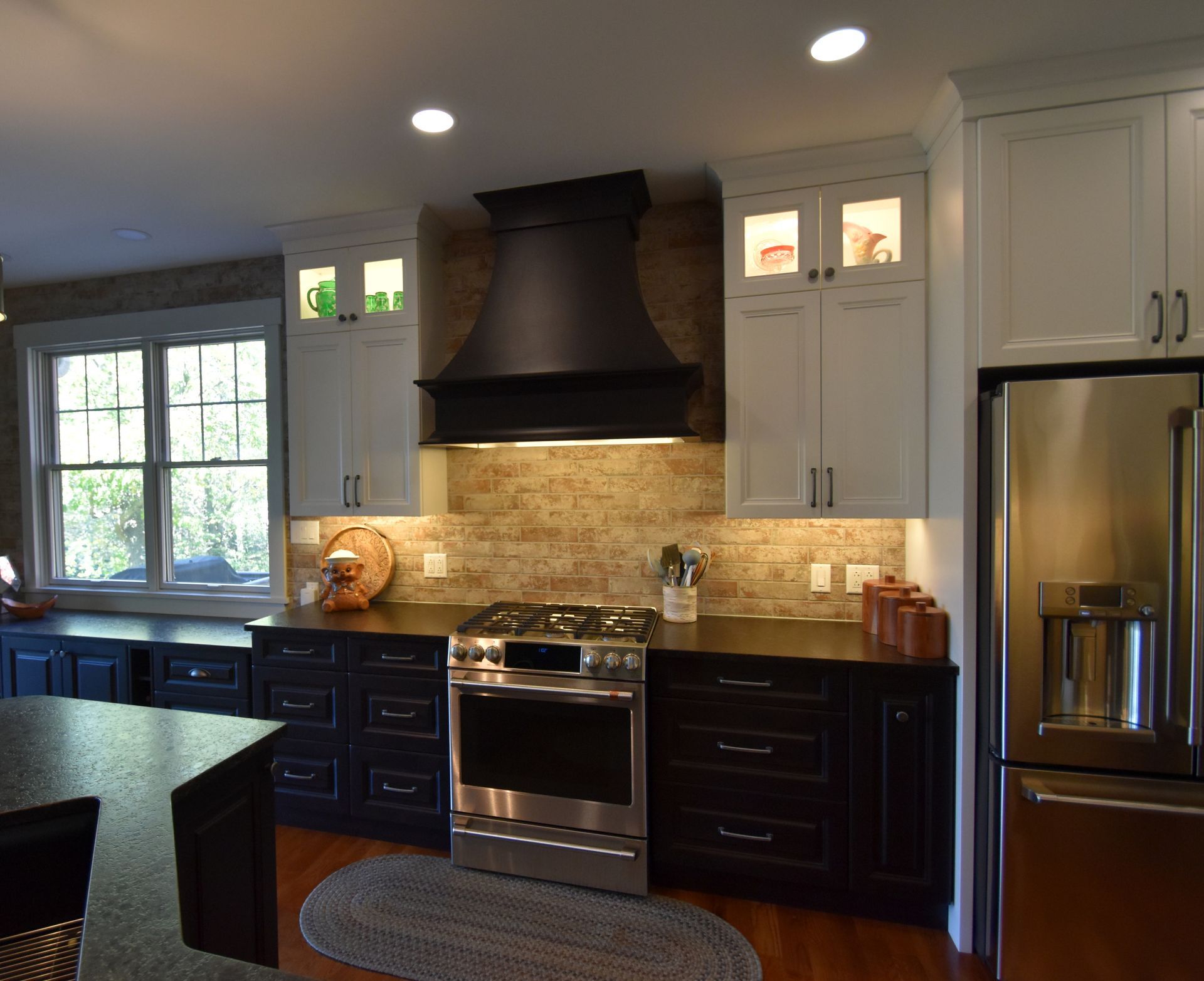 Modern kitchen with dark cabinets, stainless steel appliances, island, and stone backsplash, lit by recessed lights