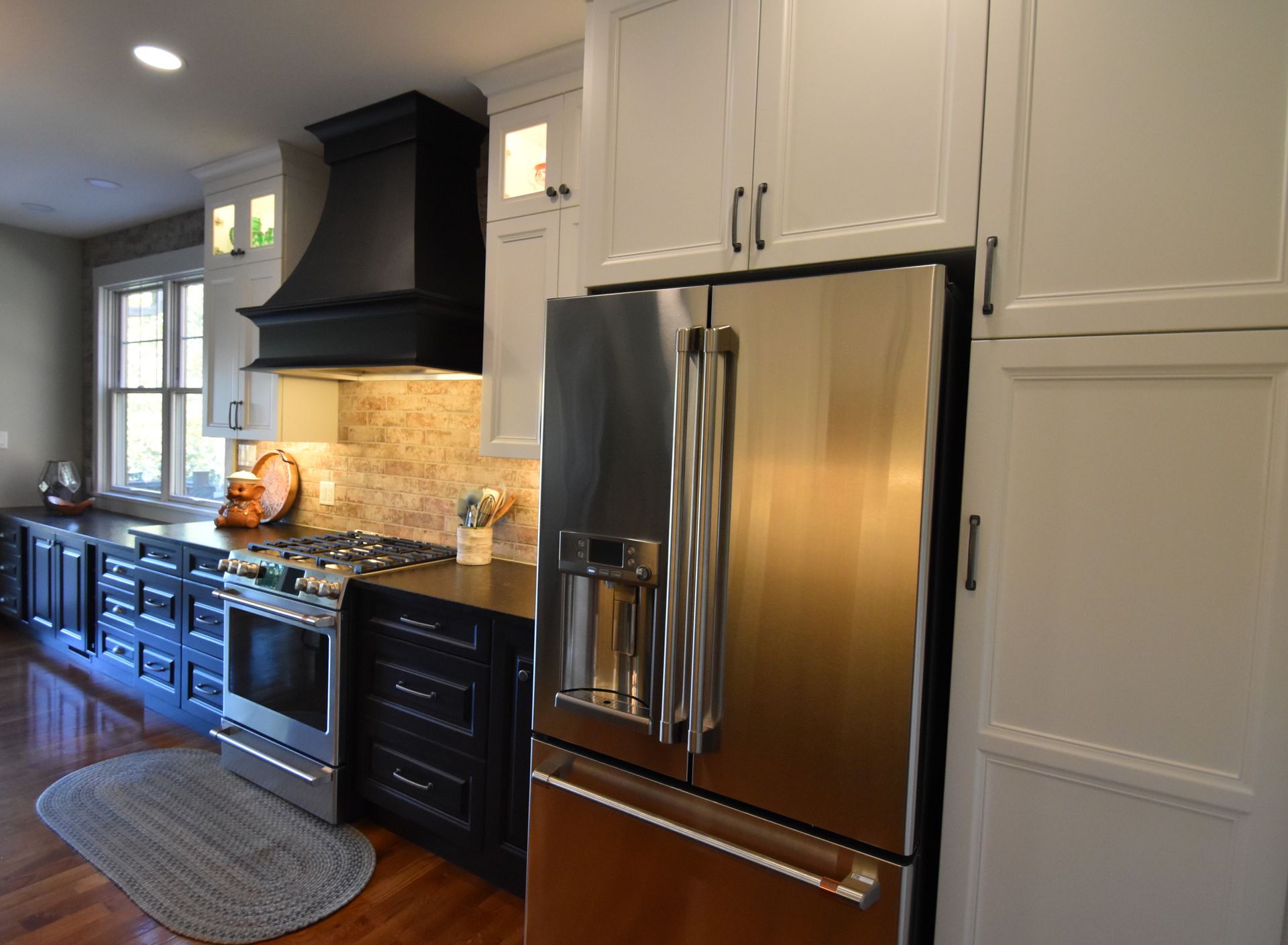 Modern kitchen with white cabinets, stainless steel refrigerator, and black stove and hood